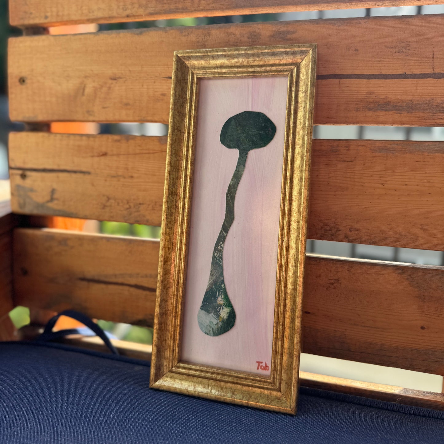 Framed abstract mushroom collage on a wooden bench.