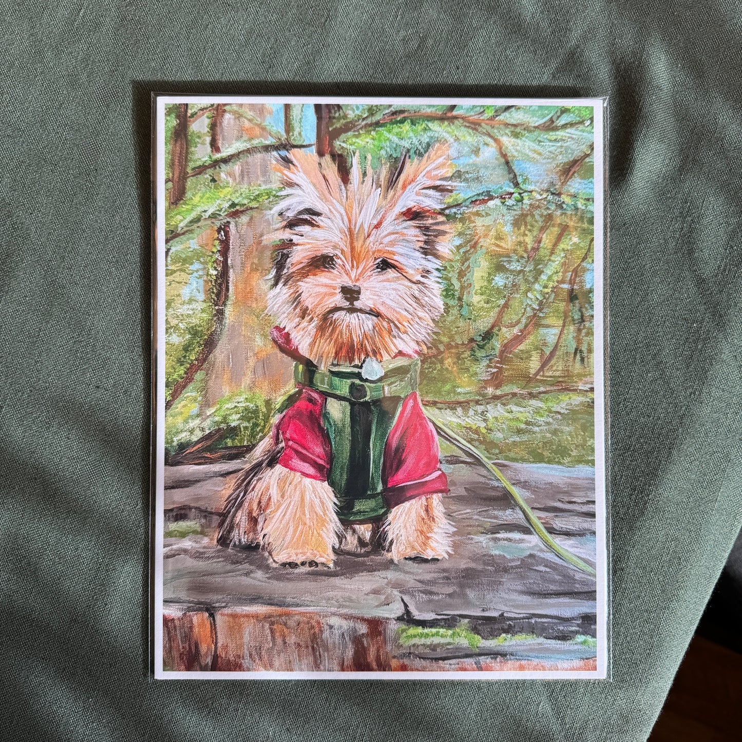Print of the small dog is shown in the artists home, on a table with a green table cloth.
