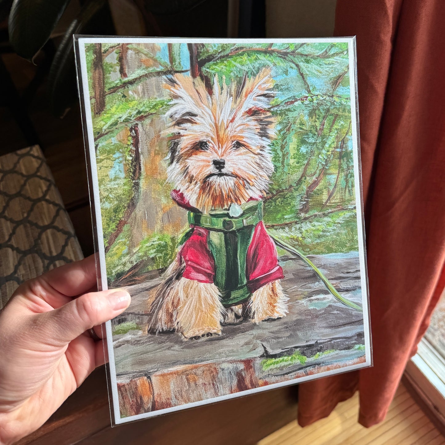 Artist holding the print in hand — featuring a cute small dog on a tree stump.