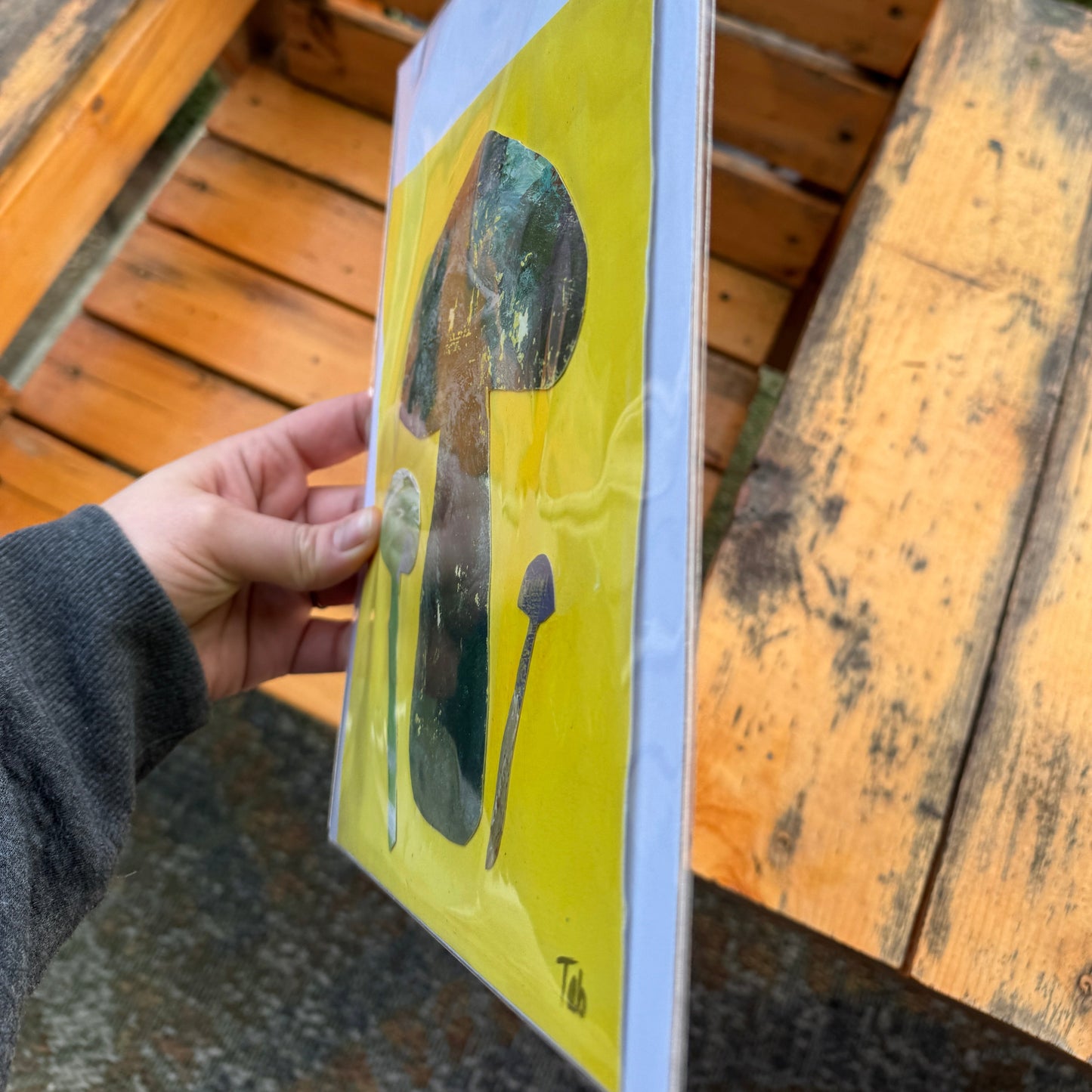 Hand holding a yellow artwork with mushroom illustrations.