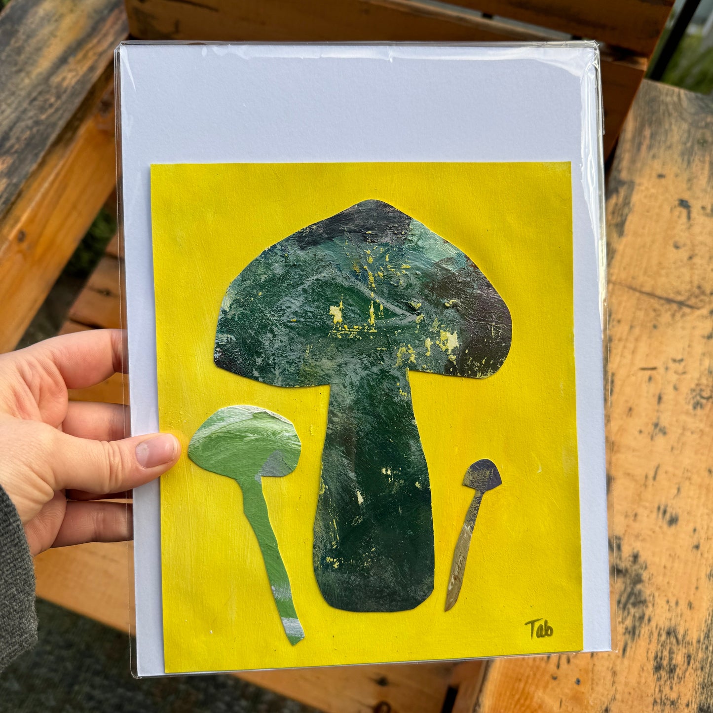 Artwork with mushroom illustrations on a yellow background held by a hand.