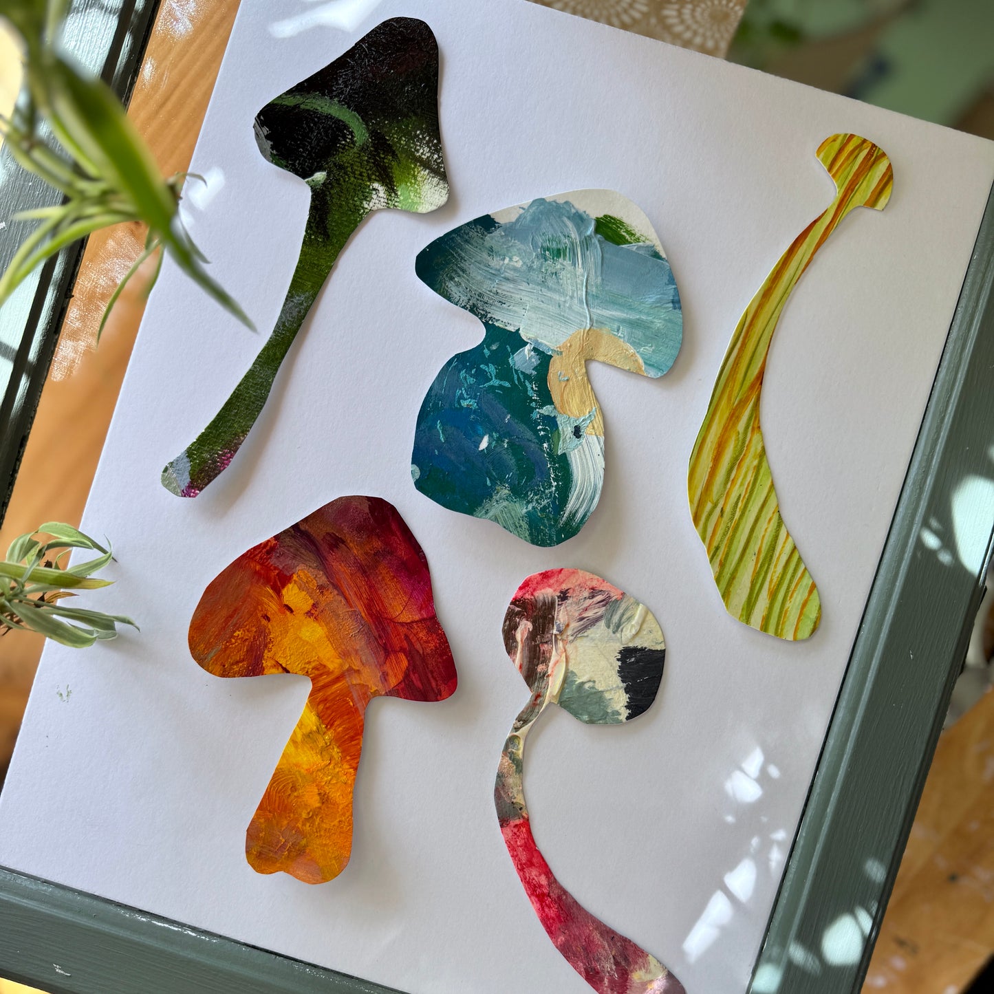 Large art stickers handmade from colorful artist palettes. The stickers are shown on a white surface with plants and wood surrounding the five large mushroom stickers.