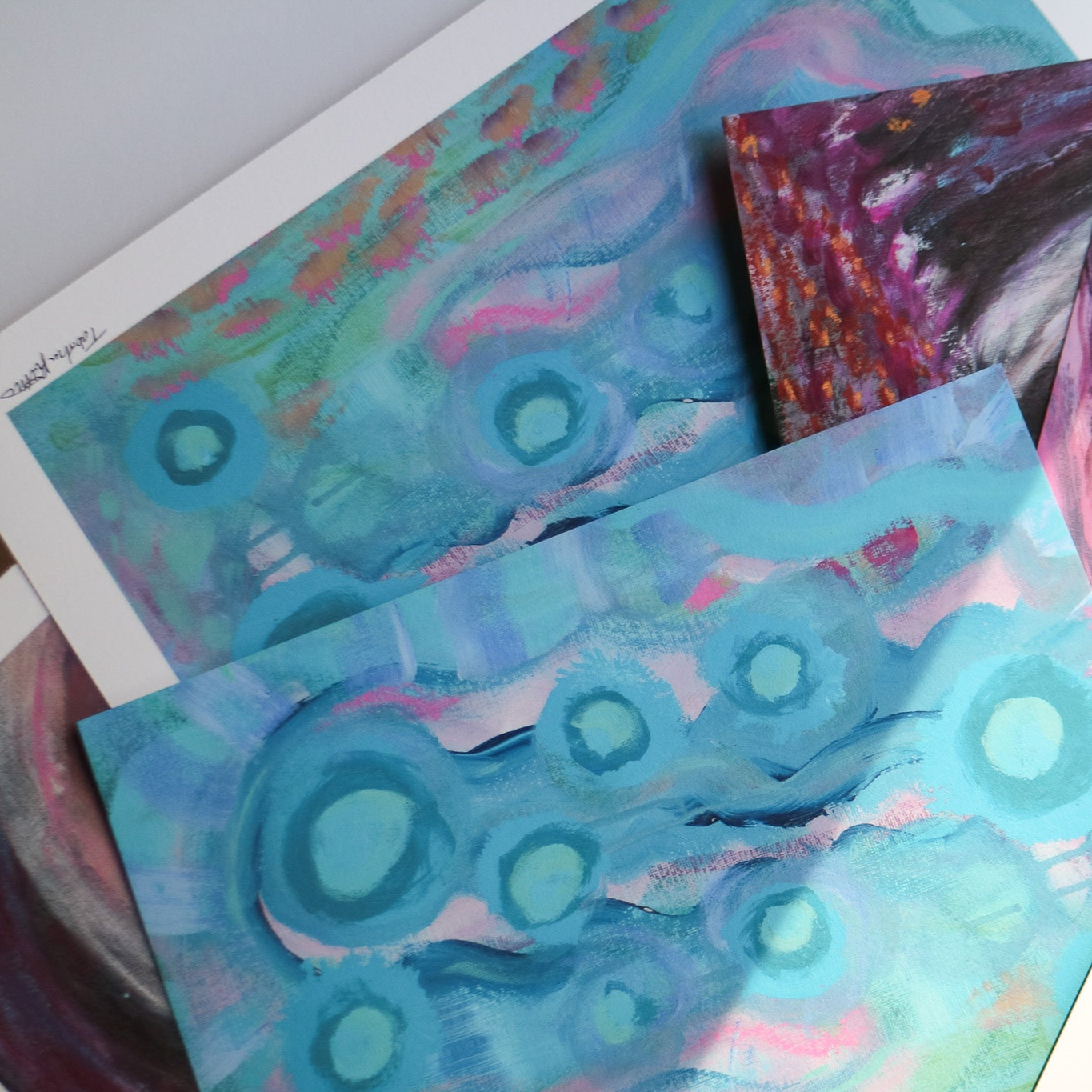 Abstract fine art prints, Your Weird is Glowing and Tunnel of Fun, are photographed artistically in the sunlight on a white background.