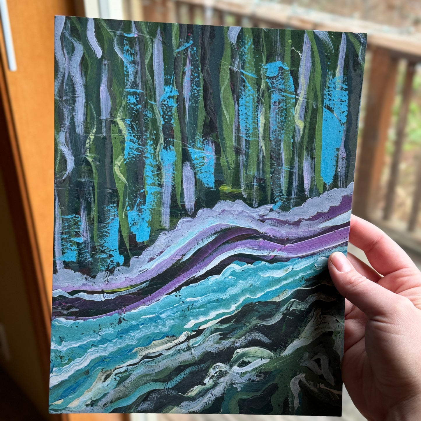 Small, abstract fine art print, By the Water, held by the artist near a window showing nature. Abstract artwork features vibrant colors, combining playful design with organic textures.