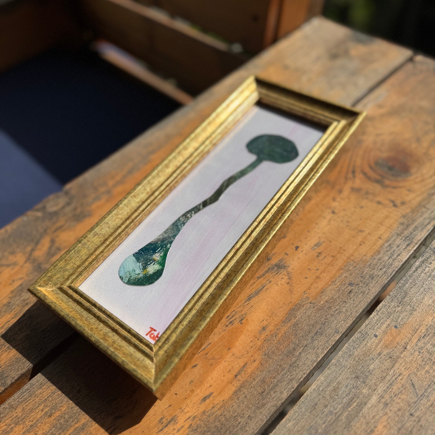 Framed collage of an abstract green mushroom on a wooden surface.