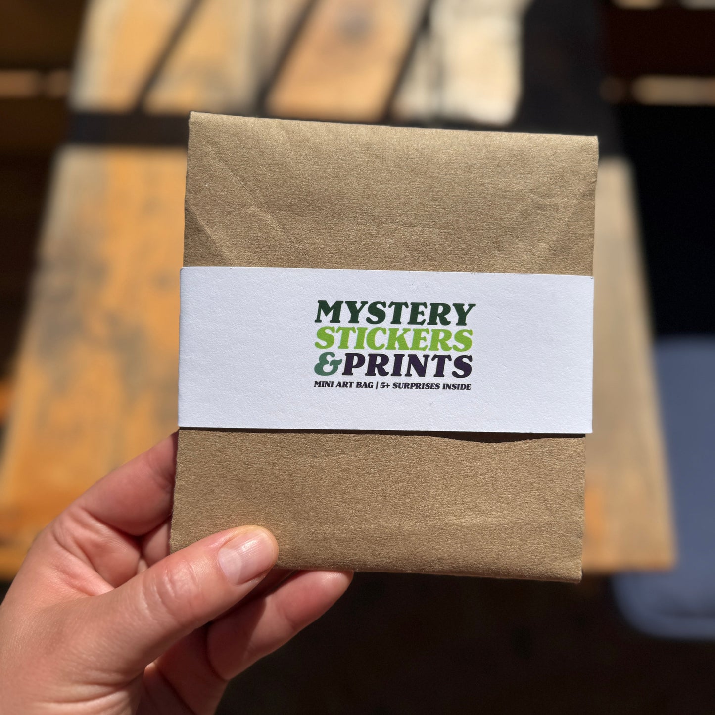 Hand holding a brown envelope with 'Mystery Stickers & Prints' label.