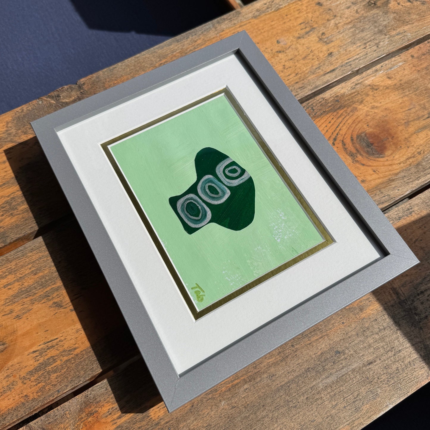 Framed artwork with a green background on a wooden surface.