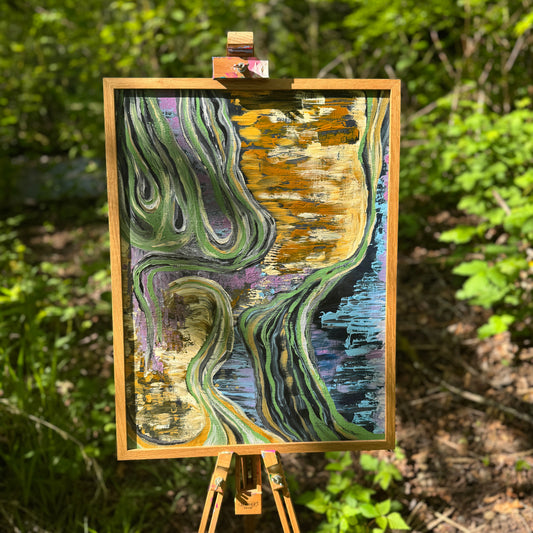 A large, earth-toned, multicolored abstract painting is shown in the woods with morning sunlight hitting it. It is displayed in a wooden frame on an artist's easel.