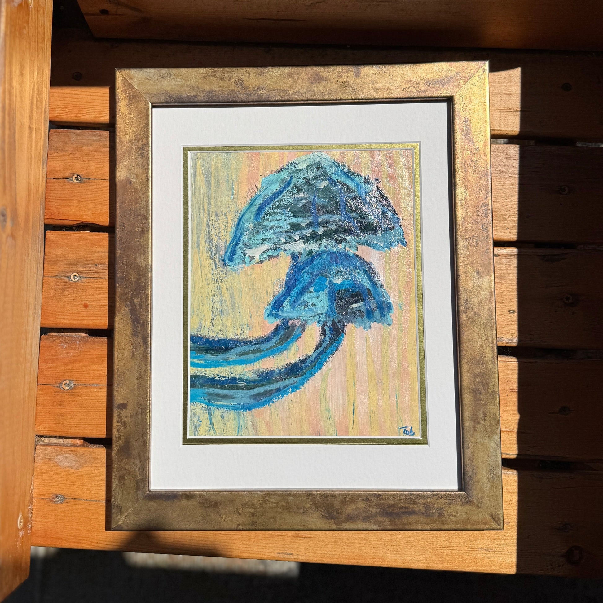 Framed artwork of a blue mushroom on a wooden surface.
