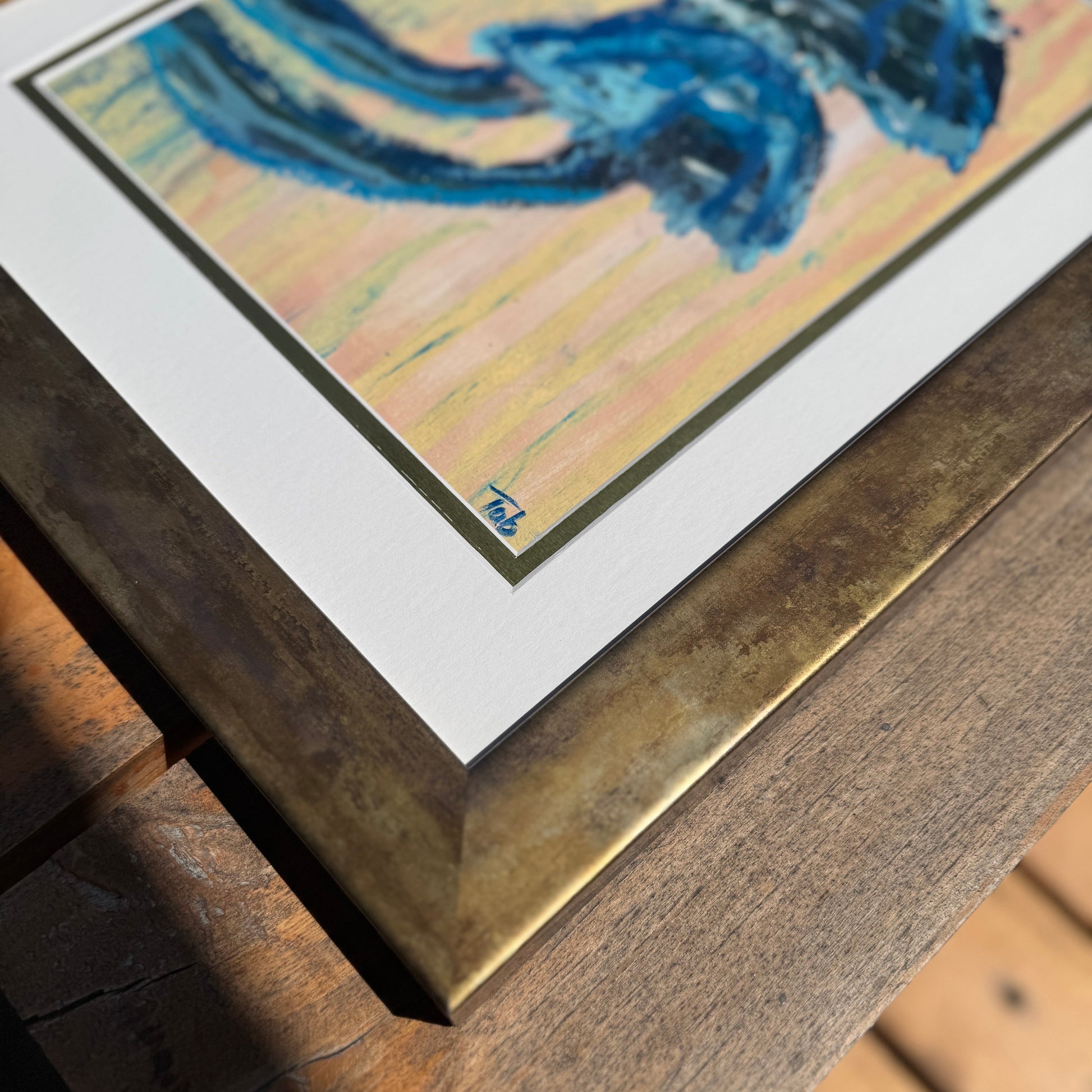 Close-up of framed artwork with a blue abstract mushroom design on a wooden surface.