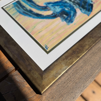 Close-up of framed artwork with a blue abstract mushroom design on a wooden surface.