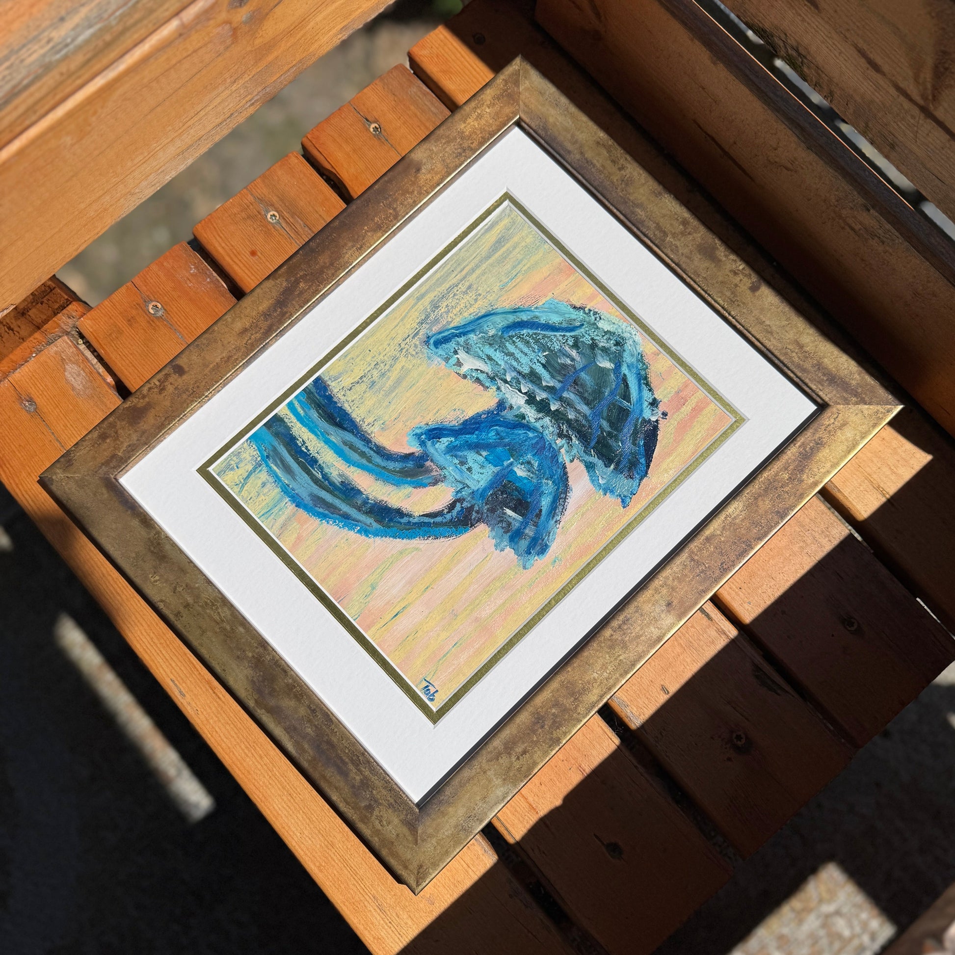 Framed artwork of a blue abstract mushroom design on a wooden surface.