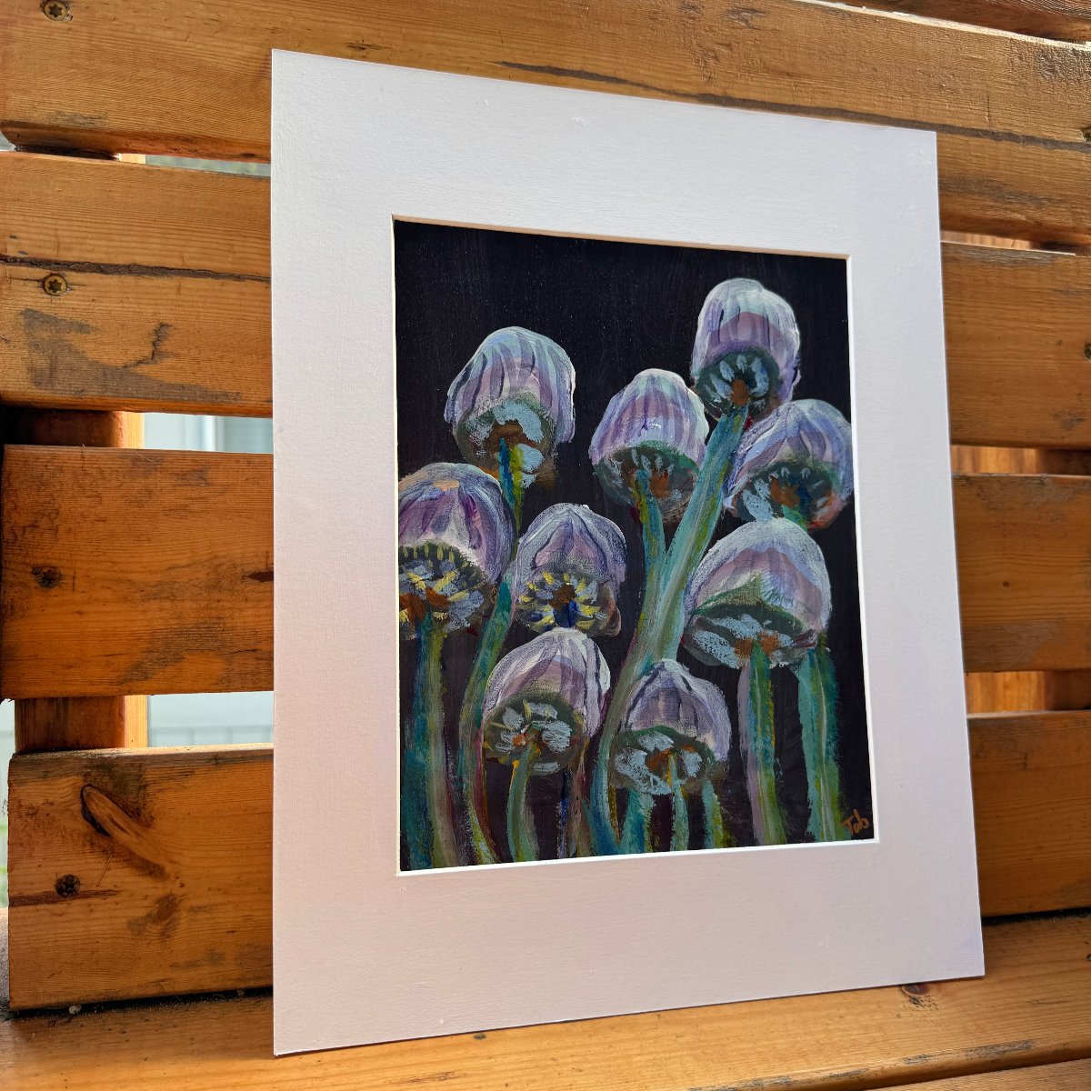 Abstract nature artwork, Mingling Mush featuring purple and green mushrooms with a white matte, unframed. The artwork is on a wooden bench outdoors on a sunlit day. 