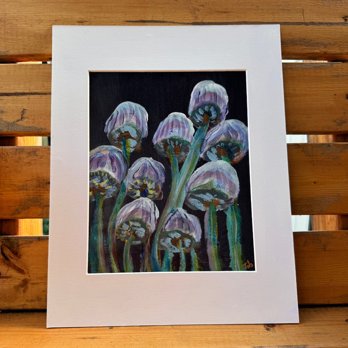 Abstract nature artwork, Mingling Mush featuring purple and green mushrooms with a white matte, unframed. The artwork is on a wooden table outdoors on a sunlit day. 