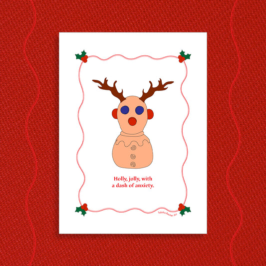 White greeting card displayed on a vibrant Holiday red felt-textured background with an illustration of the squeeze neurodivergent toy, Panic Pete, wearing festive reindeer antlers in the center of the card. Red text, under the artwork, reads: Holly, jolly, with a dash of anxiety.