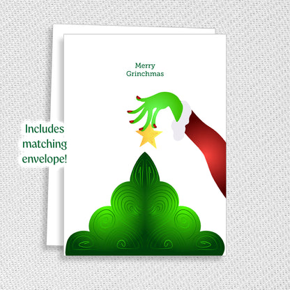 Christmas card with a green hand holding a star above a green tree, with text 'Merry Grinchmas' on a white background.