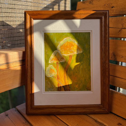 Nature-inspired, multimedia artwork, Golden Hour, on a sunny day on a wooden bench. It is displayed in a thrifted frame with a white matte.