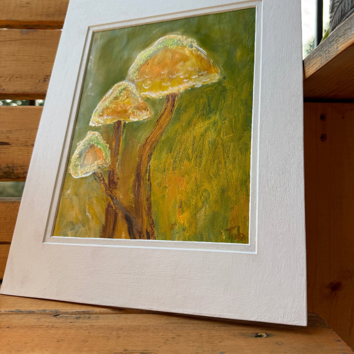 Nature-inspired, multimedia artwork, Golden Hour, on a sunny day on a wooden bench with plants. Angled shot of the artwork in the white matte. 