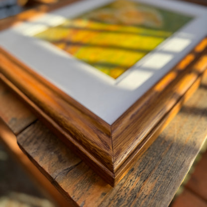 Nature-inspired, multimedia artwork, Golden Hour, on a sunny day on a wooden table. Close up of the right corner frame, showing the artistry in the refurbished thrifted frame.