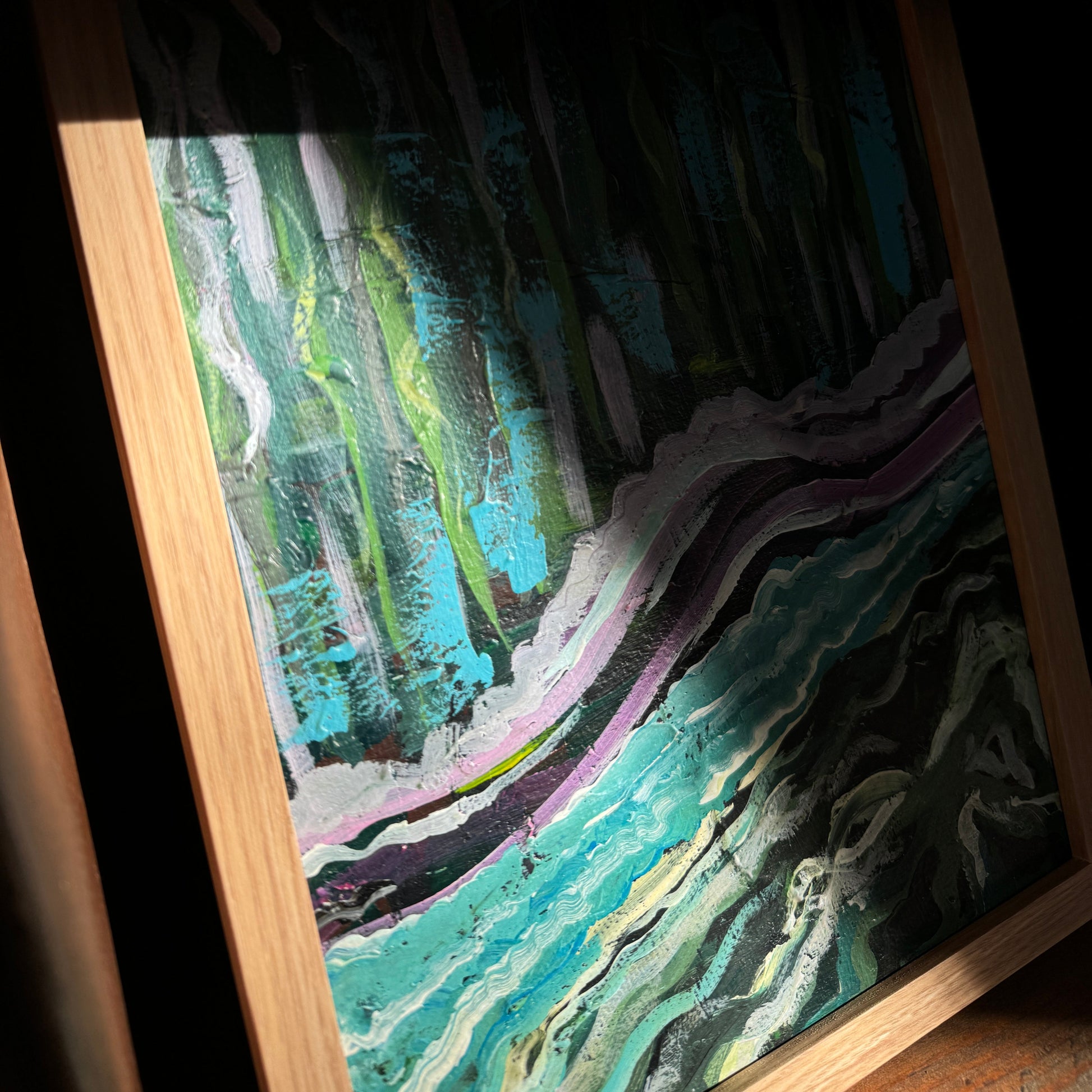 Artistically shot framed artwork in a wooden cube. The light from the window shines strongly and creates a deep shadow across the artwork and in the nook of the wood.