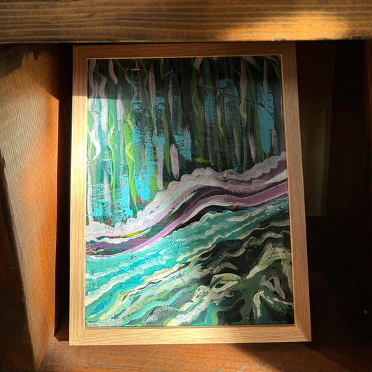 A small blue, abstract mixed media artwork, By the Water, in a wooden frame, is tucked in a wooden shelf with the sun shining on the corner, highlighting the painterly brush strokes.