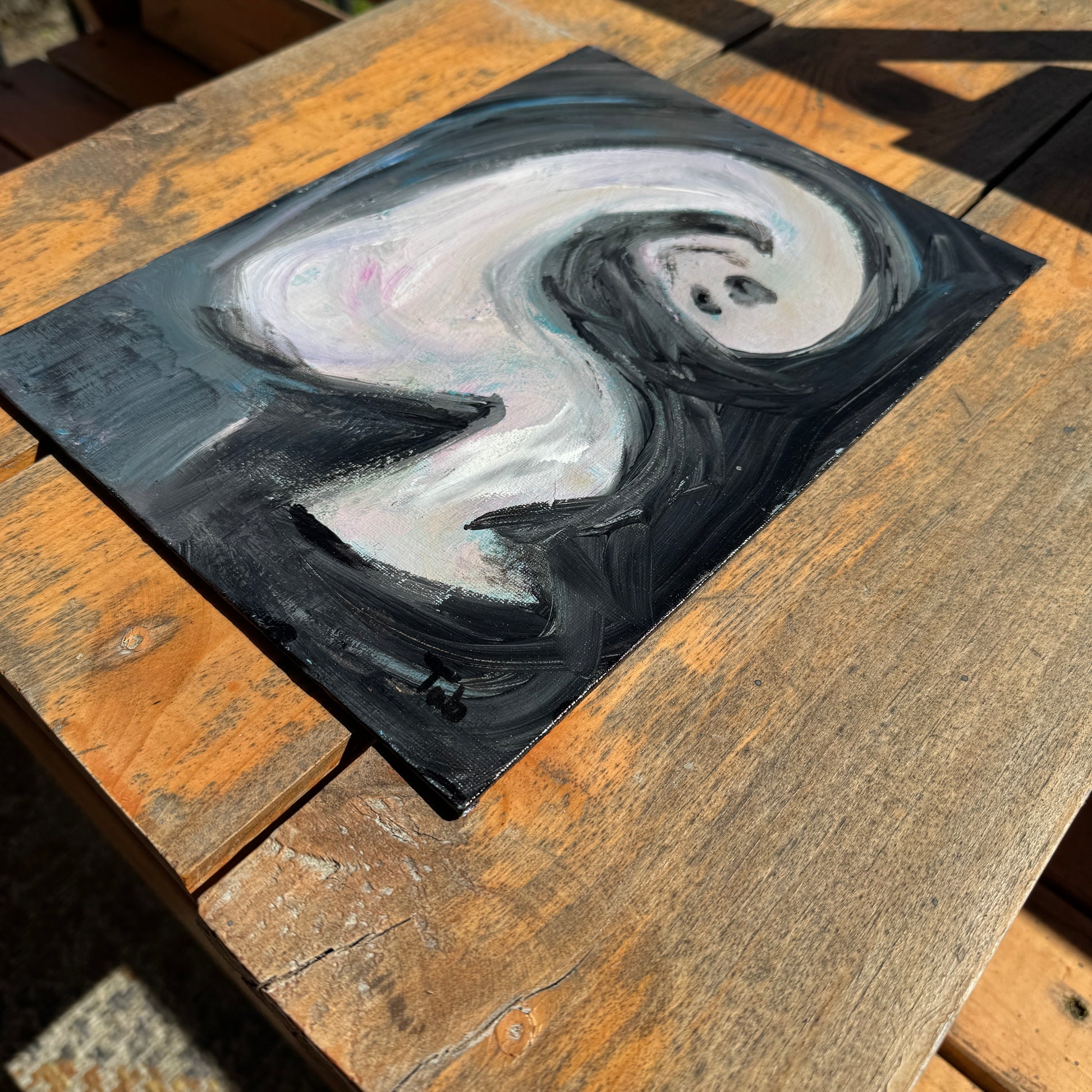 Abstract artwork, Deadlines, on a wooden table in the sun. The artwork is angled, featuring the bottom right corner with the artist’s signature.
