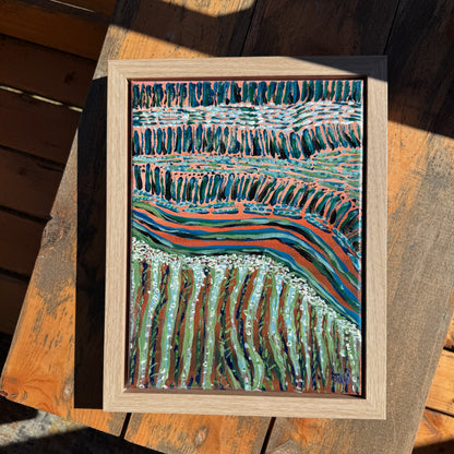 A small abstract pink and green painting on a wooden table, shining in the sunlight.