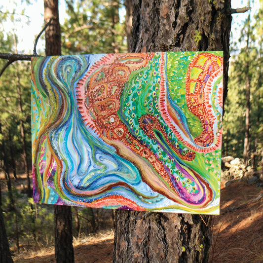 Abstract mixed media artwork, Sitting With Thoughts, balances on a tree branch in the woods. The painting is maximalist and multicolored; however, blue and orange stand out among the rest of the vibrant colors.