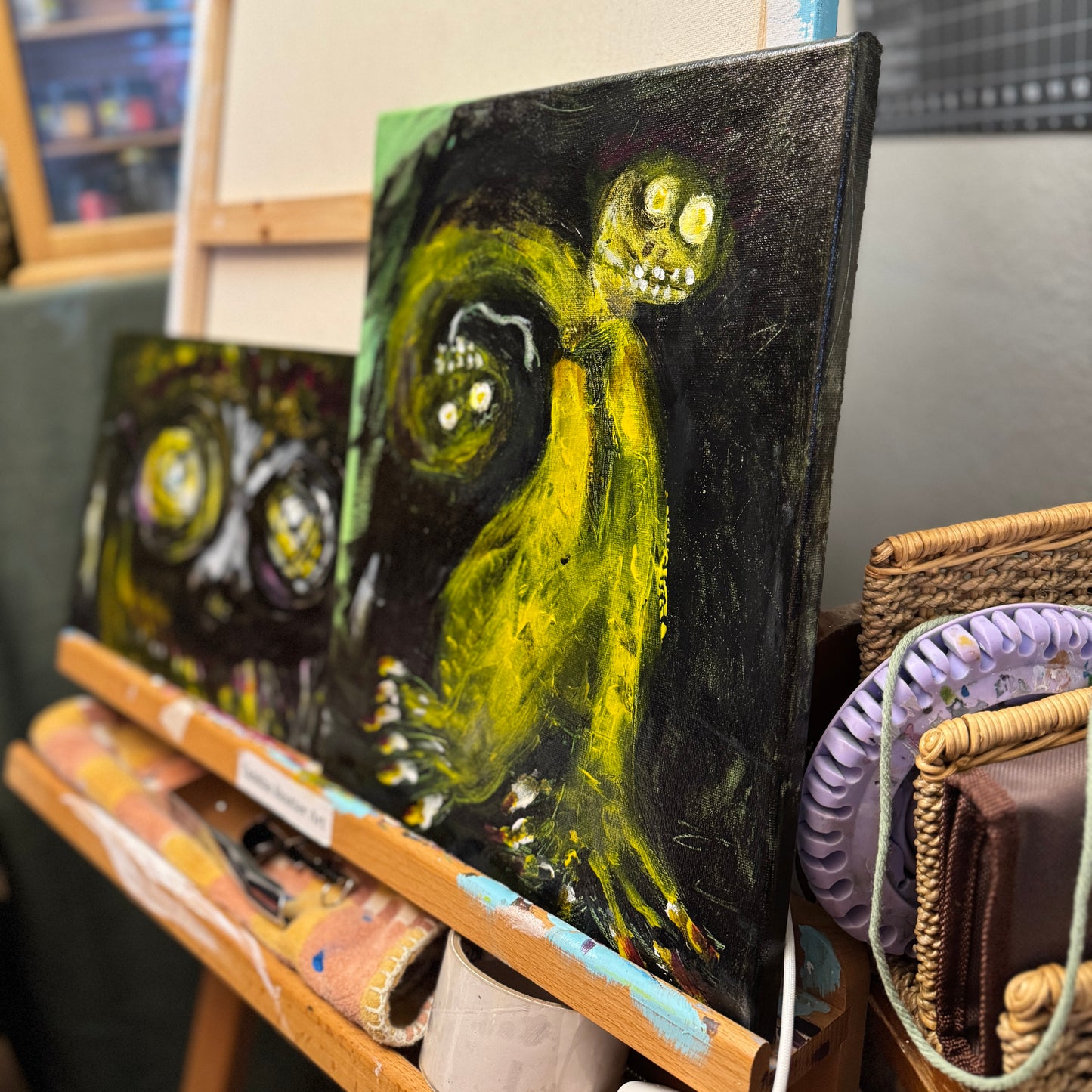 A lifestyle image of mixed-media artwork, Toxic Boss on an artist's easel. The sharp angle shows the abstract art depicting a green two-headed creature with sharp nails on a black background.