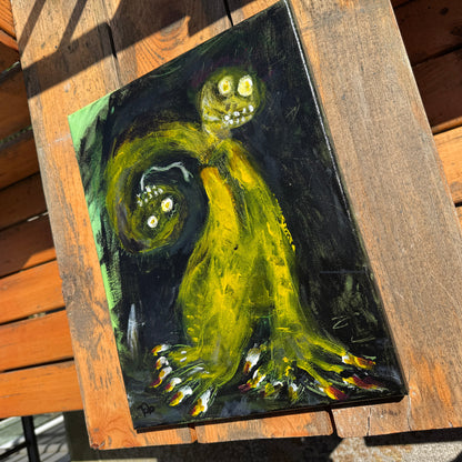 Mixed-media artwork, Toxic Boss, on a sunlit wooden table. The strong angle highlights the uncanny abstract art depicting a green two-headed creature with sharp nails on a black background.