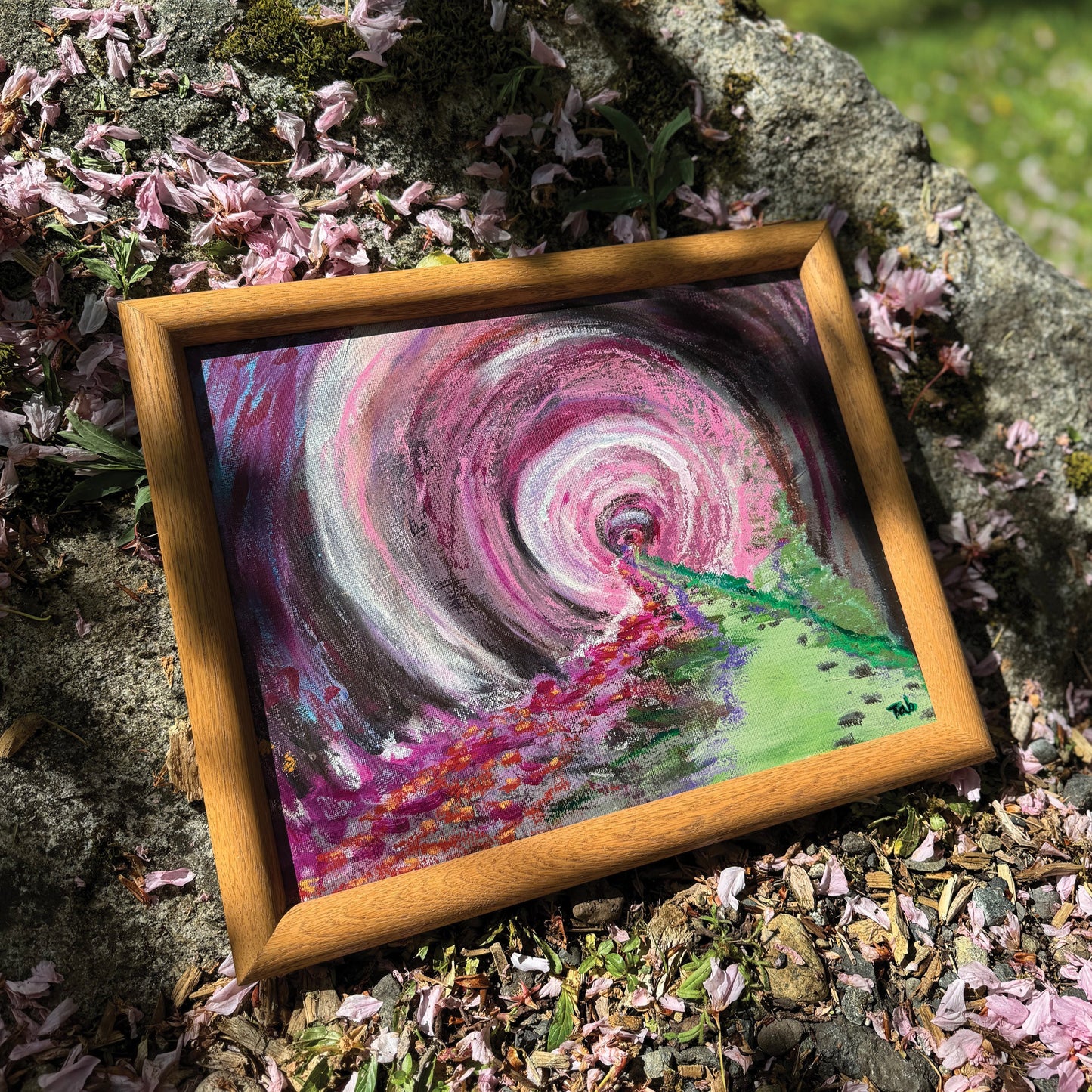 A radial abstract painting featuring lilac and green hues. The painting ays on a bed of fallen pink petals on a rock outside.