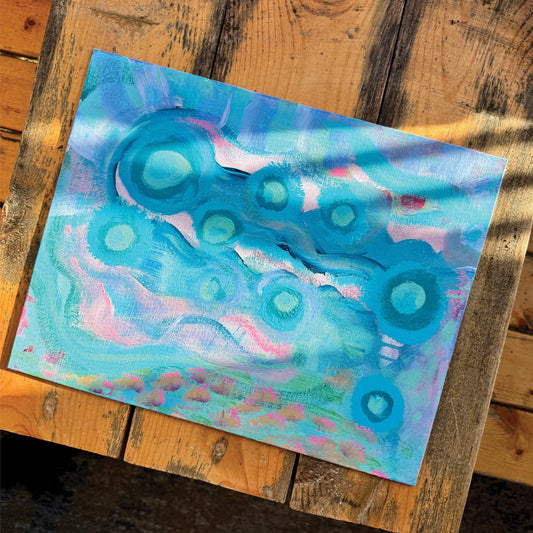 Abstract artwork, Your Weird is Glowing, on a wooden bench in the sunlight. Baby blue and pink colors intermingle, creating a whimsical effect.