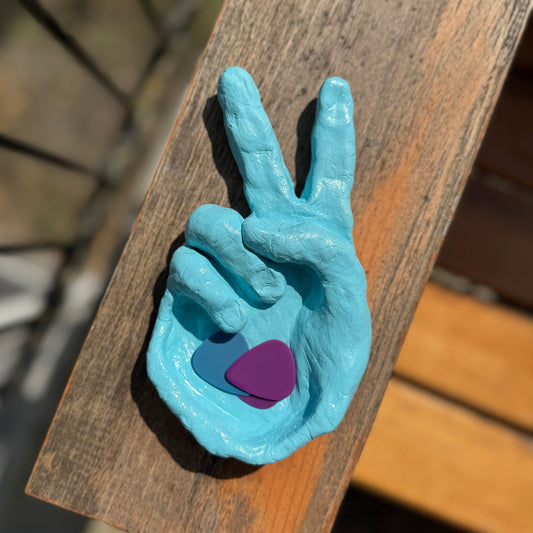 Blue hand-shaped dish with a purple guitar pick on a wooden surface