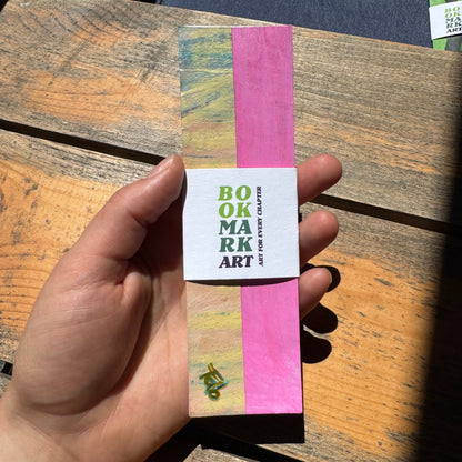 Hand holding a colorful bookmark with 'Bookmark Art' text on a wooden surface.