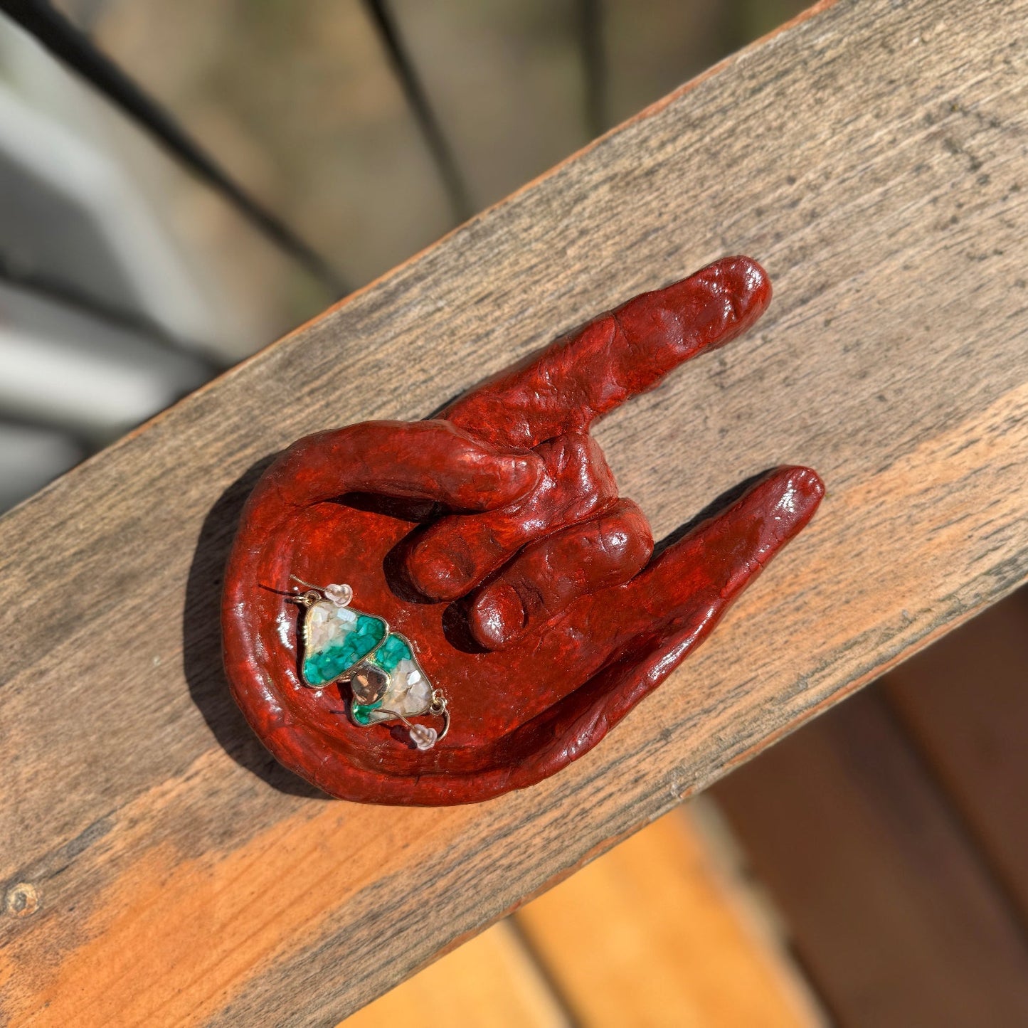 Ceramic red hand dish holding teal earrings on a wood surface.