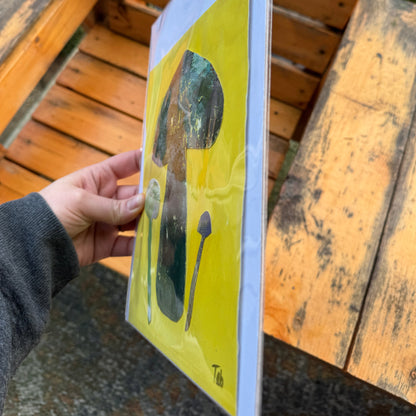 Hand holding a yellow artwork with mushroom illustrations.
