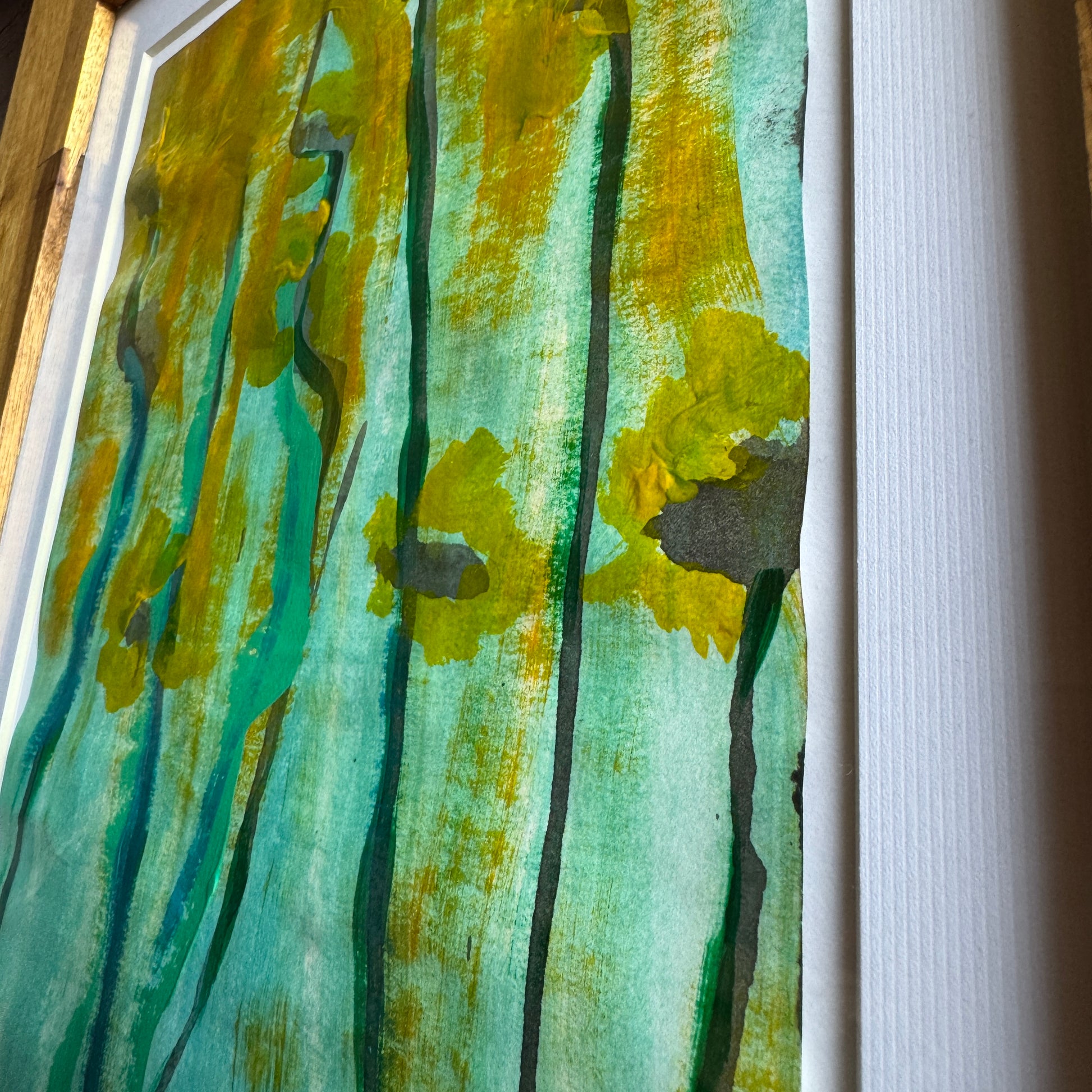 Close up of framed artwork with abstract design in green, yellow, and black on a white background