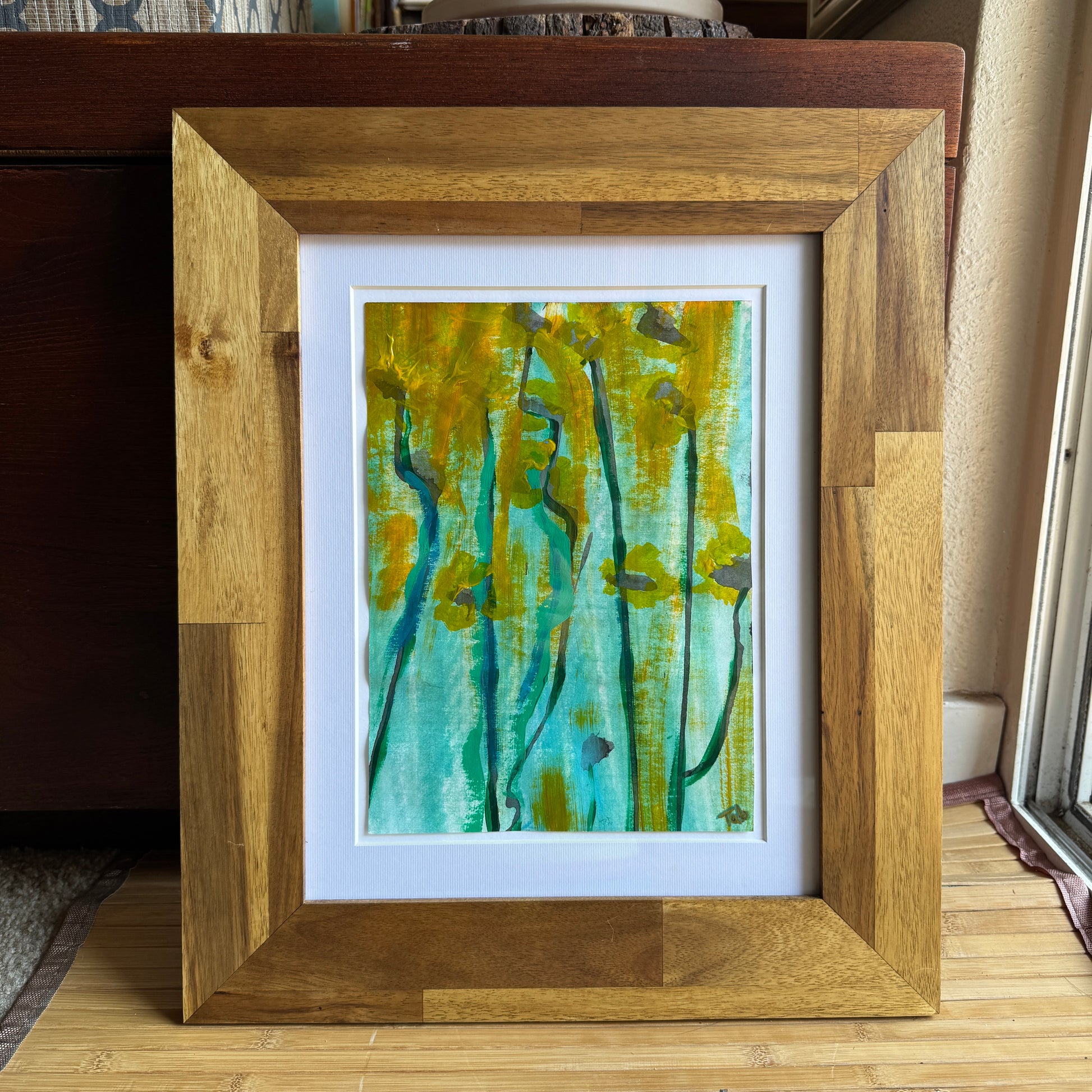 Framed artwork with a natural wood frame on a wooden chest in art studio.