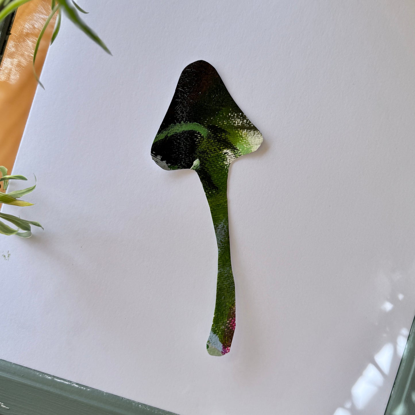 Mushroom art sticker handmade from color pallets. The sticker is placed on a white surface with spider plants peaking, adding a natural appearance.