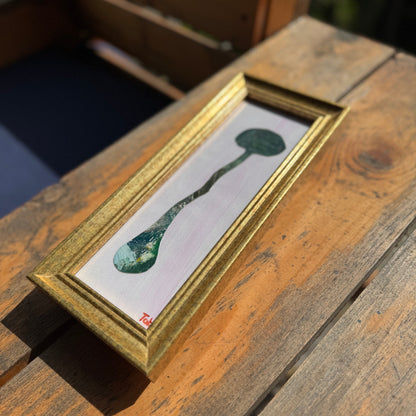 Framed collage of an abstract green mushroom on a wooden surface.