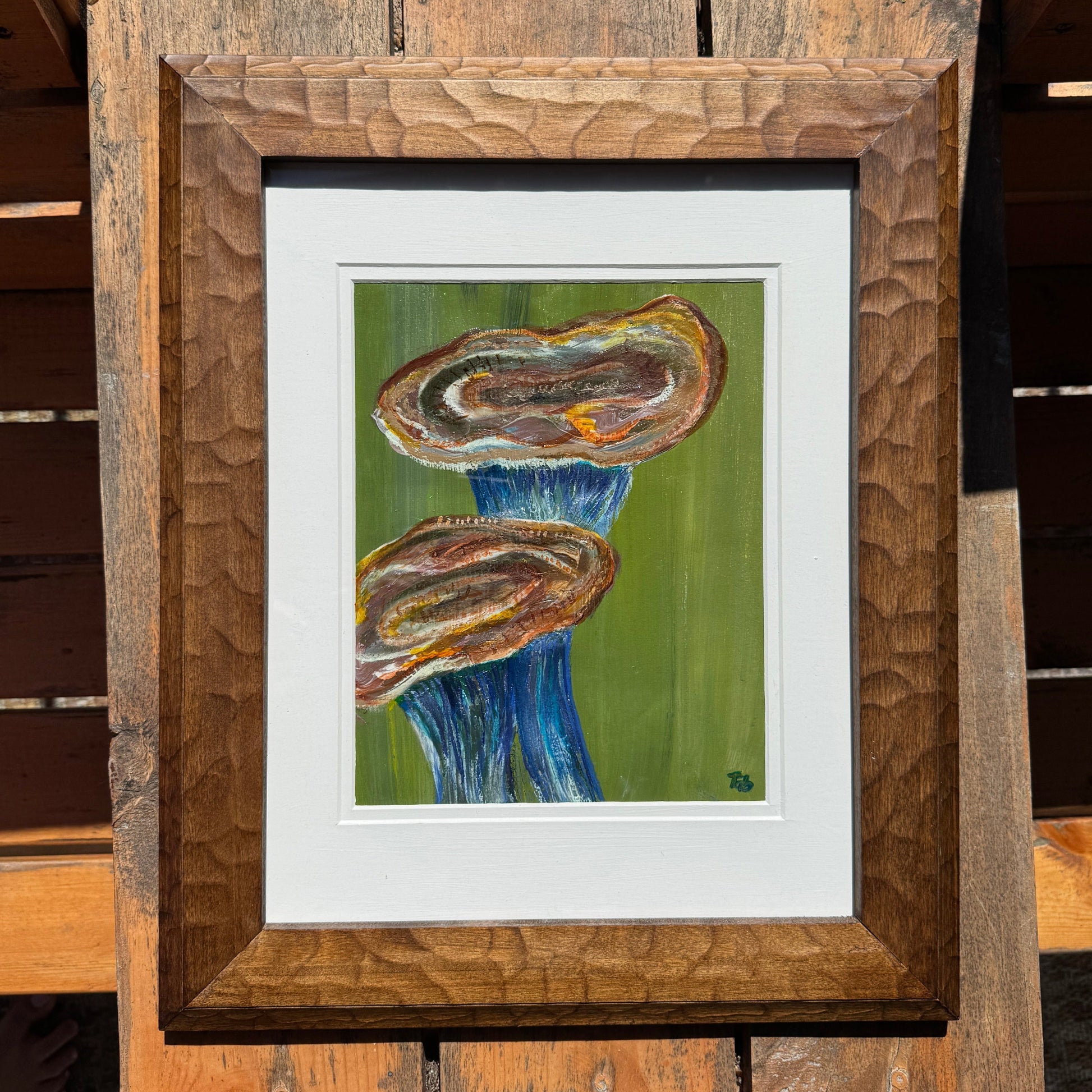Framed artwork of an abstract blue and orange mushroom on a wooden surface