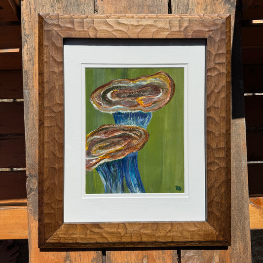Framed artwork of an abstract blue and orange mushroom on a wooden surface
