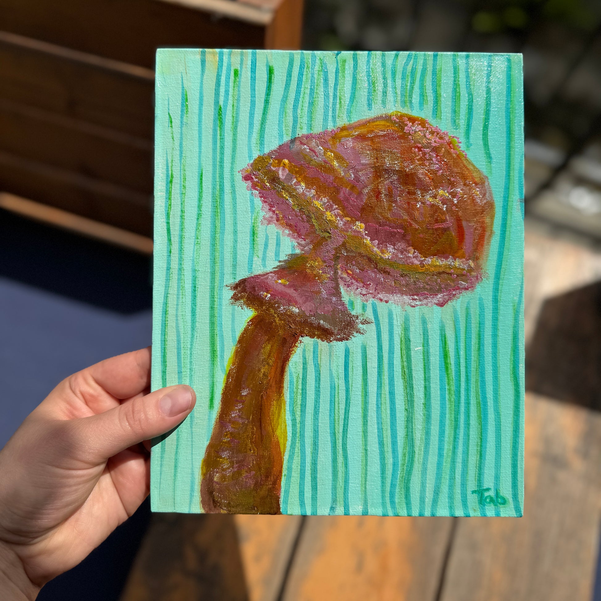 Hand holding a small painting of a mushroom on a textured green background