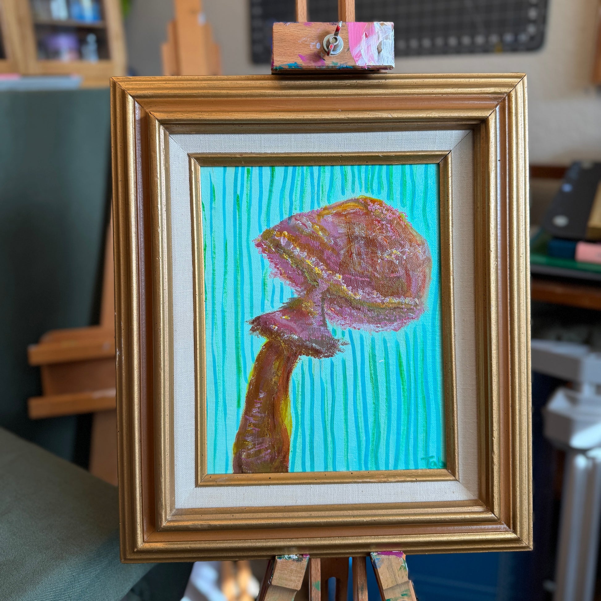 Framed artwork of a colorful mushroom on an easel with a blurred indoor background
