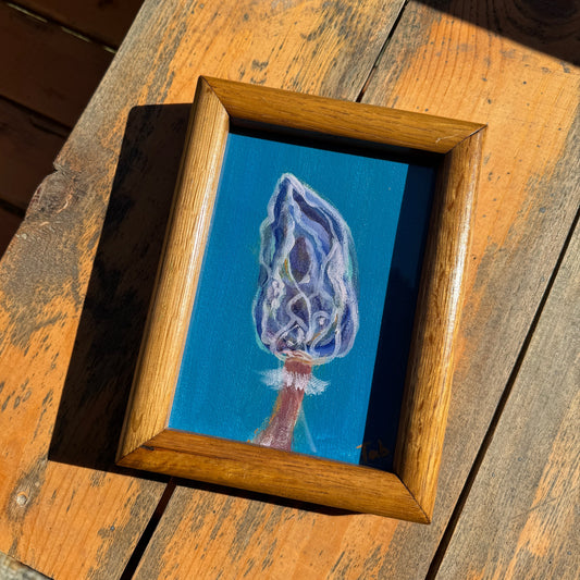 Framed artwork of a blue mushroom in a thrifted wood frame on a wooden surface.