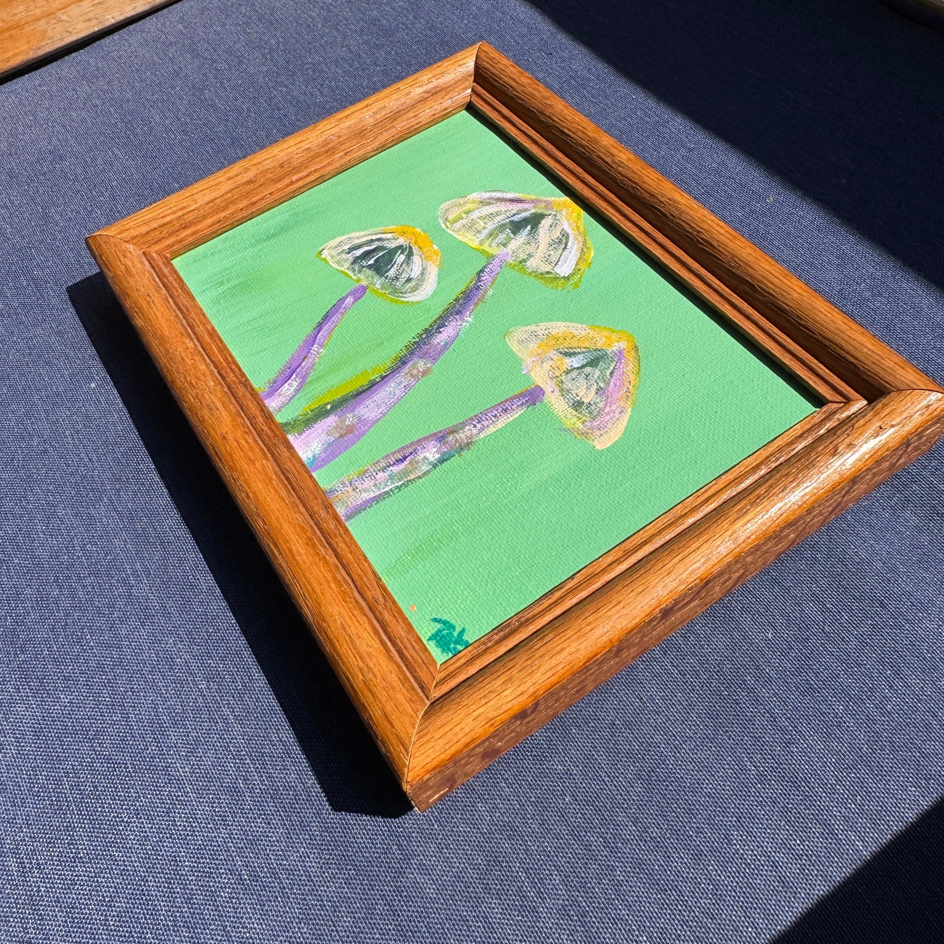 Wooden-framed painting of mushrooms on a blue background.