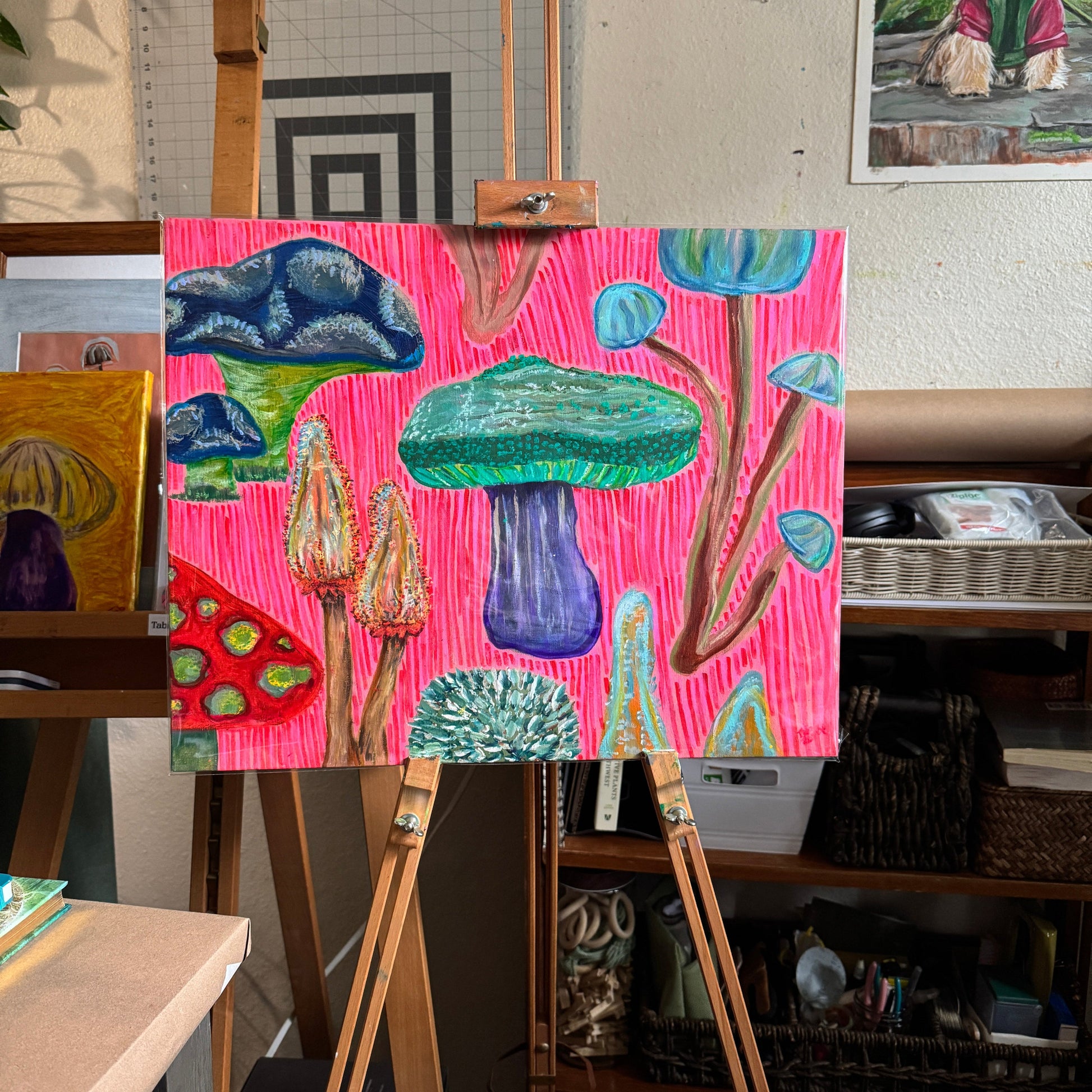 Colorful multimedia artwork Fun Fungi is displayed on an easel in the artist's studio. Bold hot pink background and magenta lines create a graphic look to the art.
