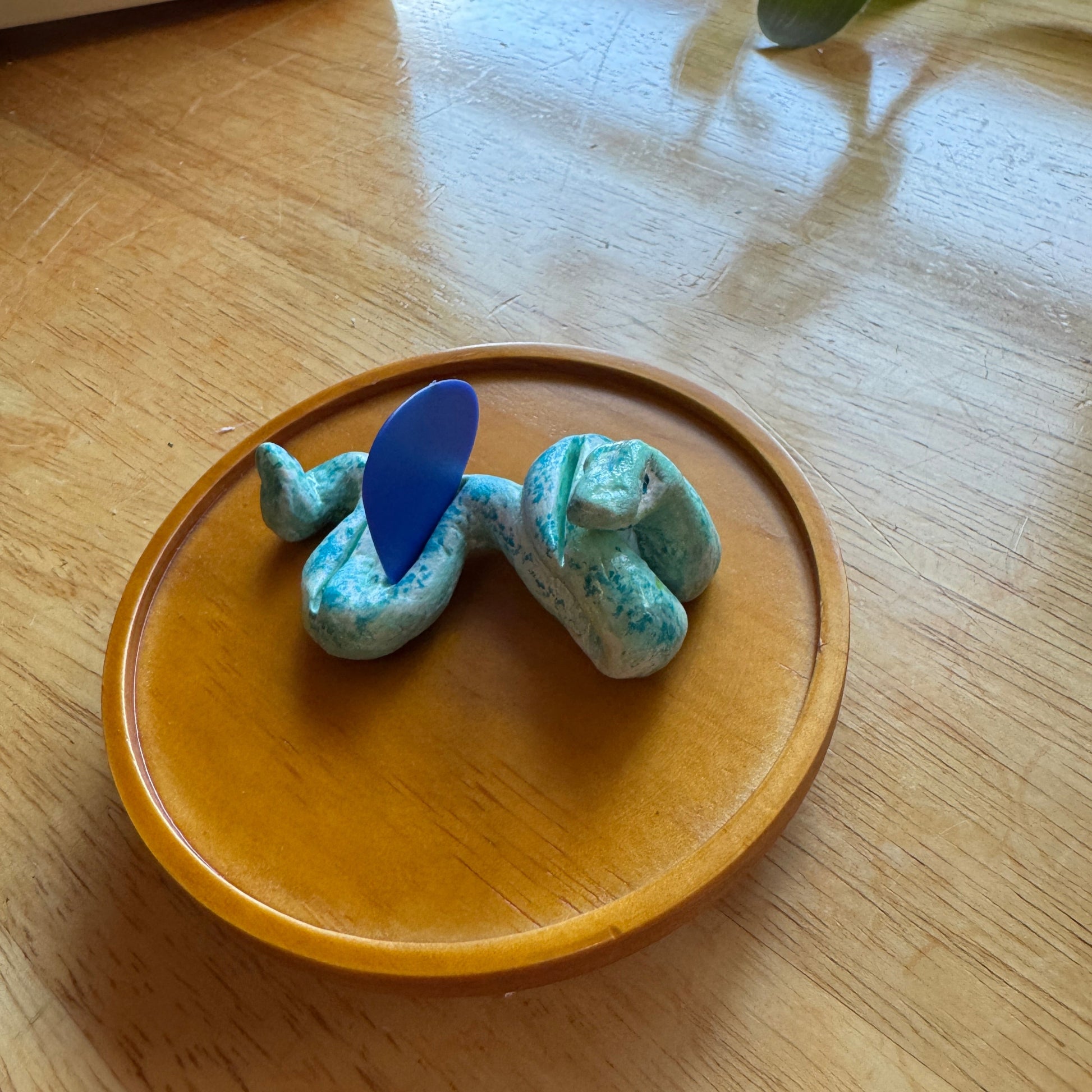 Blue and green snake-shaped guitar pick holder on a wooden plate