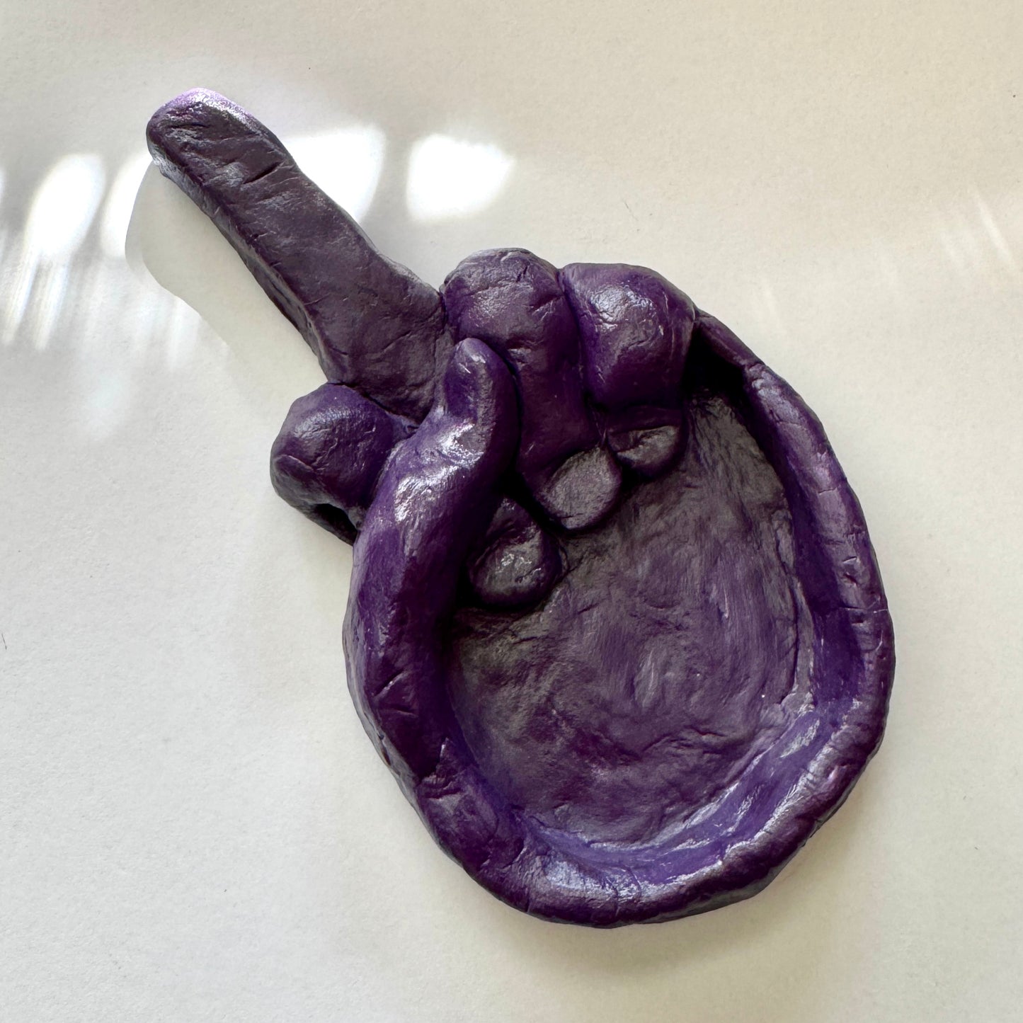 Purple clay sculpture of a hand on a white surface