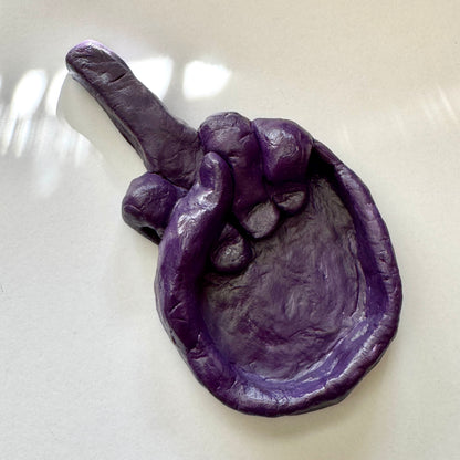 Purple clay sculpture of a hand on a white surface